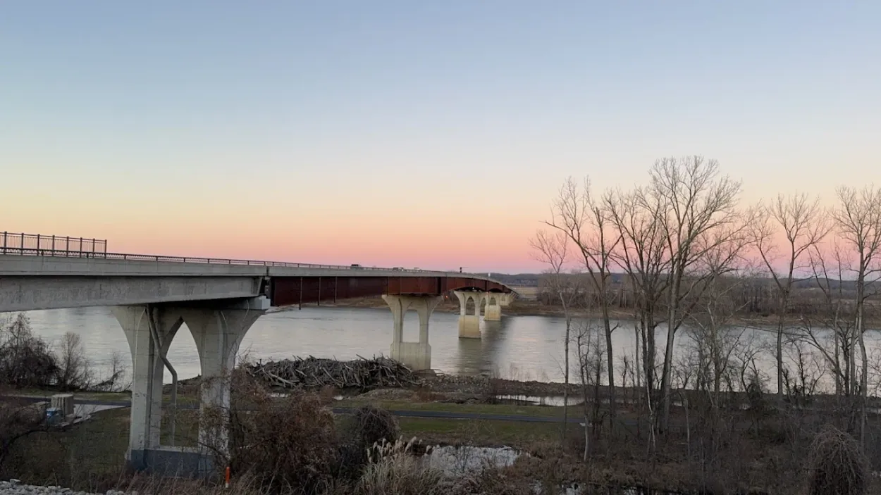 # Alt Text

Sunset over calm river with bare trees and bridge in distance
