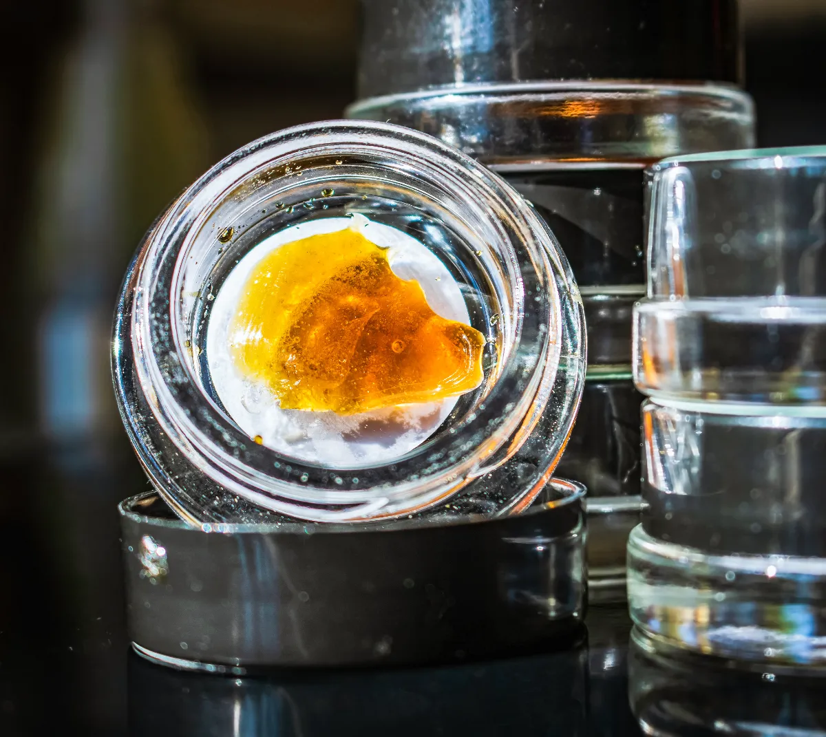 Cannabis concentrate with golden amber color in glass container on reflective surface