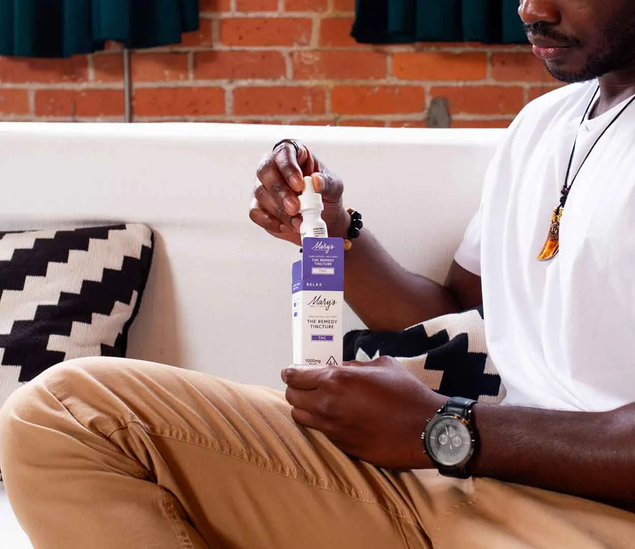 # Alt Text

Person holding purple cannabis product bottle in home setting with brick wall background